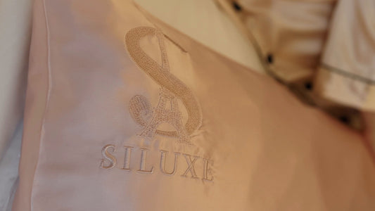 A close-up of a Rose gold silk pillowcase with its embroidered S monogram and SILUXE wordmark
