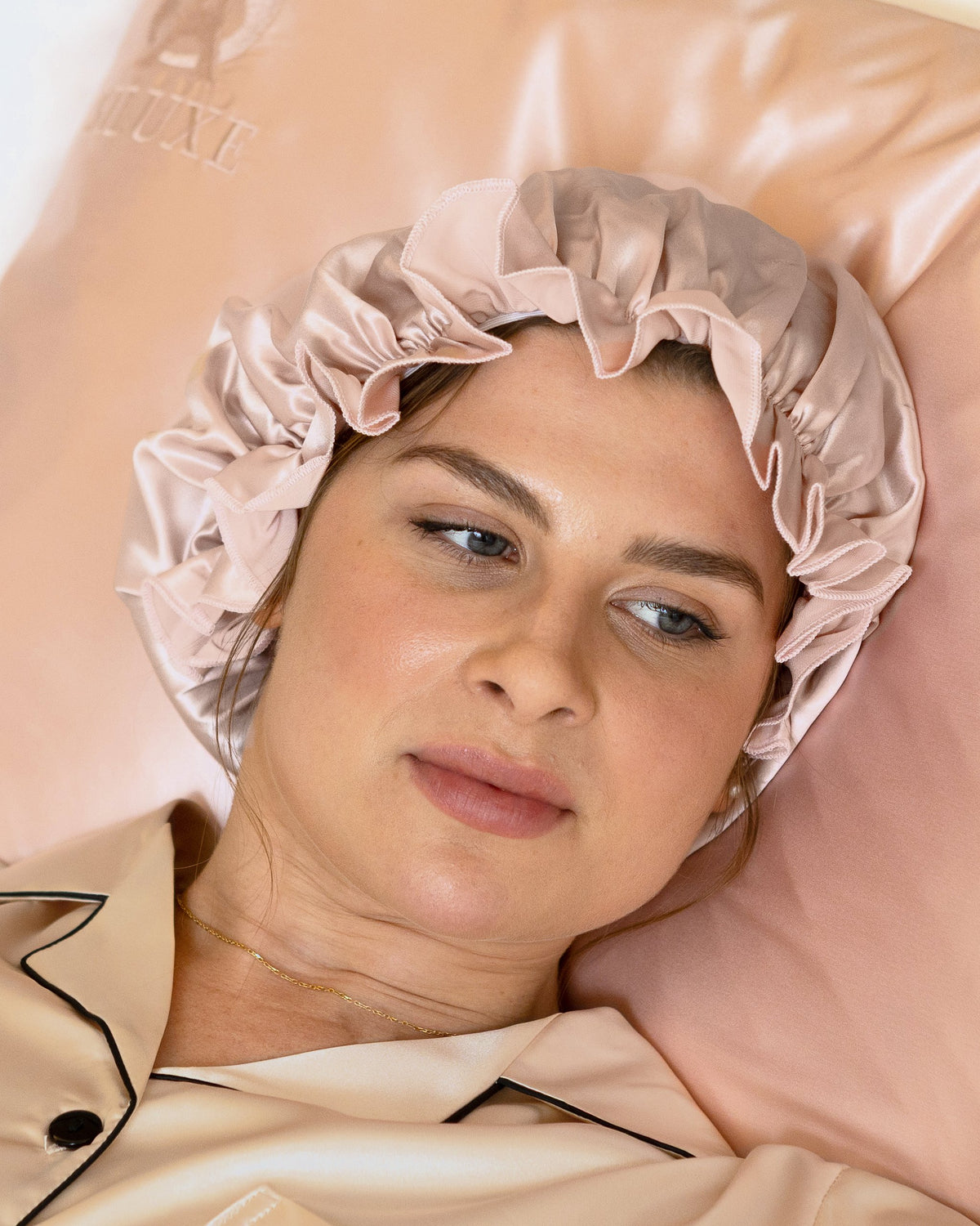 Gathered ruffle of the Siluxe Comfort silk bonnet in Rose gold, gaze away, hand on the pillow