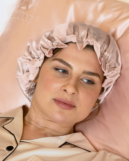 Gathered ruffle of the Siluxe Comfort silk bonnet in Rose gold, gaze away, hand on the pillow