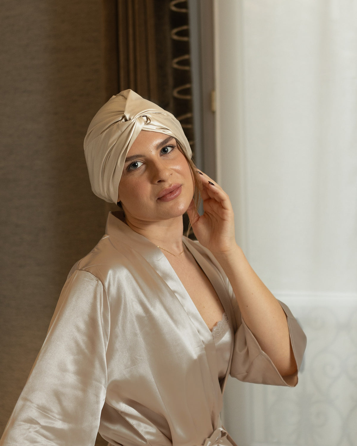 Siluxe Glow silk bonnet in Gold worn sitting on the bed, soft smile, before bedtime