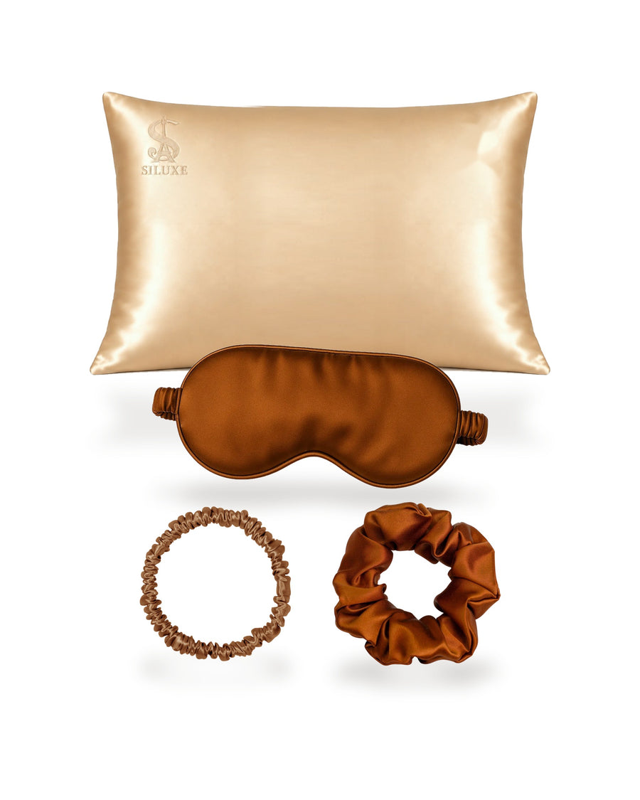 Siluxe GiftBox in Bronze, the four pieces shown without the box: a Gold silk pillowcase (Standard 50 × 70 cm shown), with a Bronze silk eye mask, scrunchie M and scrunchie L