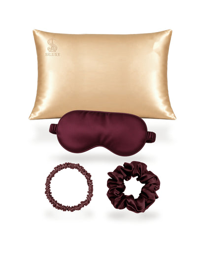 Siluxe GiftBox in Burgundy, the four pieces shown without the box: a Gold silk pillowcase (Standard 50 × 70 cm shown), with a Burgundy silk eye mask, scrunchie M and scrunchie L