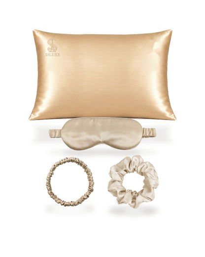 Siluxe GiftBox in Gold, the four pieces shown without the box: a silk pillowcase (Standard 50 × 70 cm shown), a silk eye mask, a scrunchie M and a scrunchie L, all in Gold