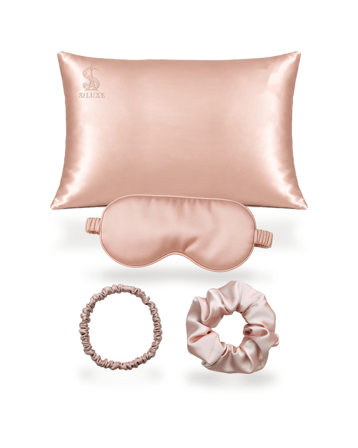 Siluxe GiftBox in Rose gold, the four pieces shown without the box: a silk pillowcase (Standard 50 × 70 cm shown), a silk eye mask, a scrunchie M and a scrunchie L, all in Rose gold
